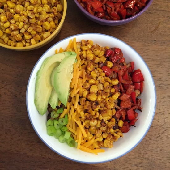 burrito bowl topped with corn, red pepper, avocado, and green onion