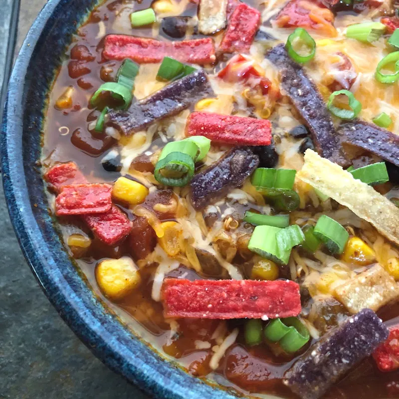 vegetarian taco soup in a bowl topped with cheese, green onions, and tortilla strips