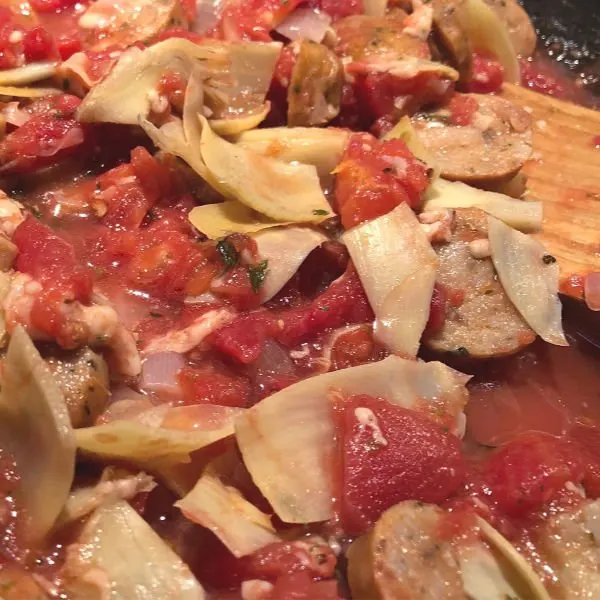 adding artichokes and tomatoes to chicken sausage in a pan