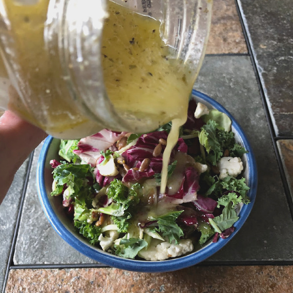 pouring artichoke marinade salad dressing onto a salad