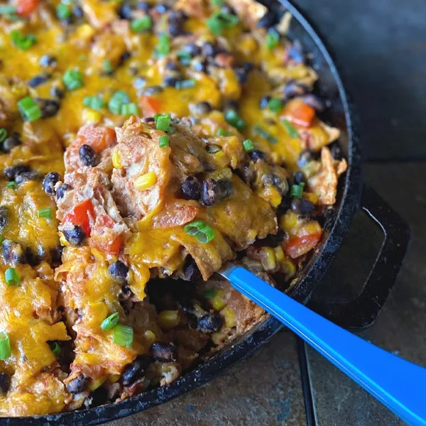Mix it up on your next Meatless Monday or Taco Tuesday with this filling & flavorful Deconstructed Vegetarian Enchiladas Skillet recipe. This cast iron skillet recipe is so easy, and naturally gluten free! Spooning out servings of the vegetarian enchiladas skillet with a blue spoon