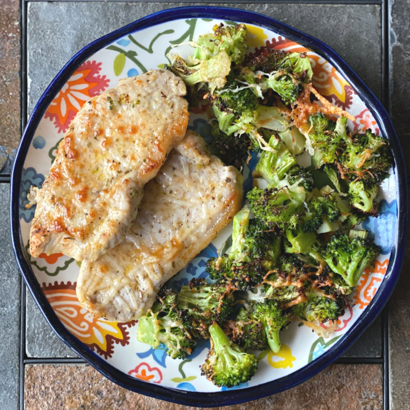 Plate of pork chops and broccoli topped with Parmesan cheese