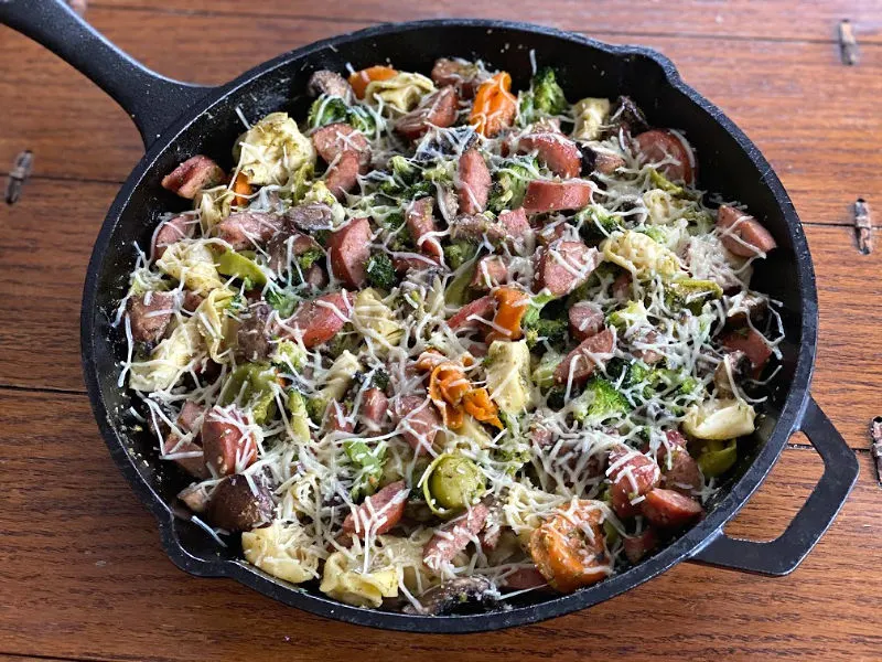 Skillet full of tortellini sausage and veggies with Parmesan on top