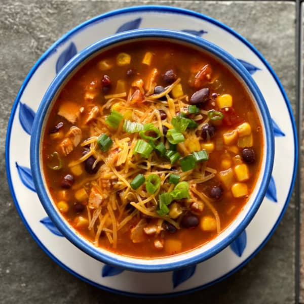 Bowl of leftover chicken taco soup, topped with shredded cheddar cheese and chopped green onion