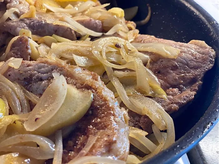 apples and onions on pork chops in a pan