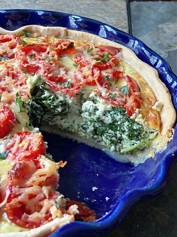 spinach, ricotta, and tomato quiche with a slice cut out