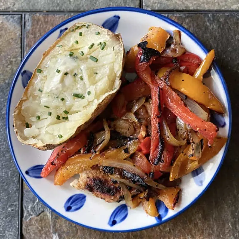 plate of pork chops with peppers and a baked potato