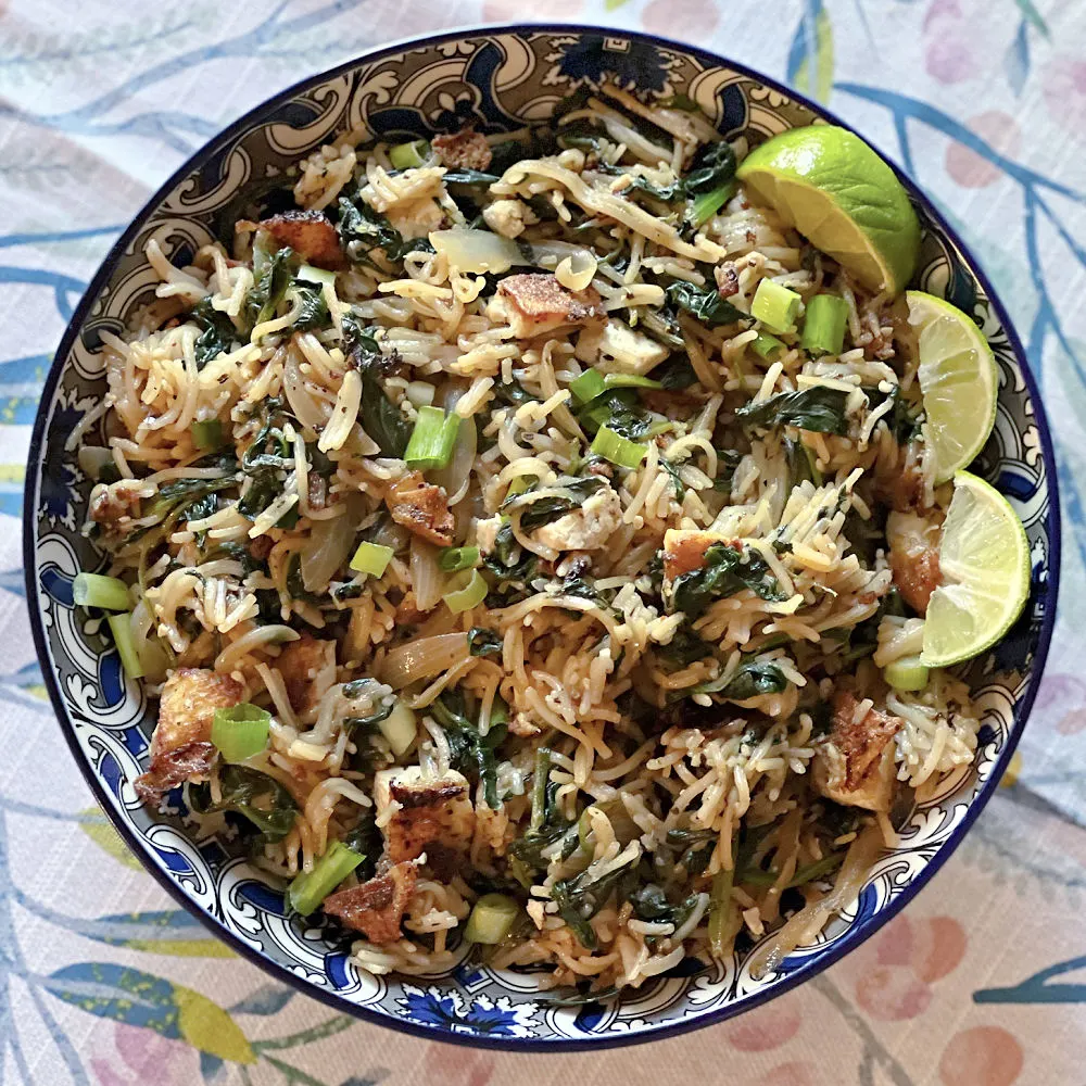 bowl of noodles with fried tofu and wilted spinach, topped with lime wedges