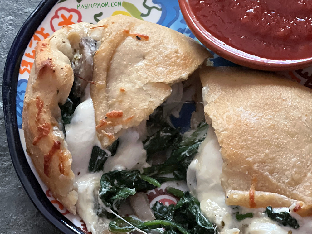 plate of very cheesy spinach calzone with dipping marinara
