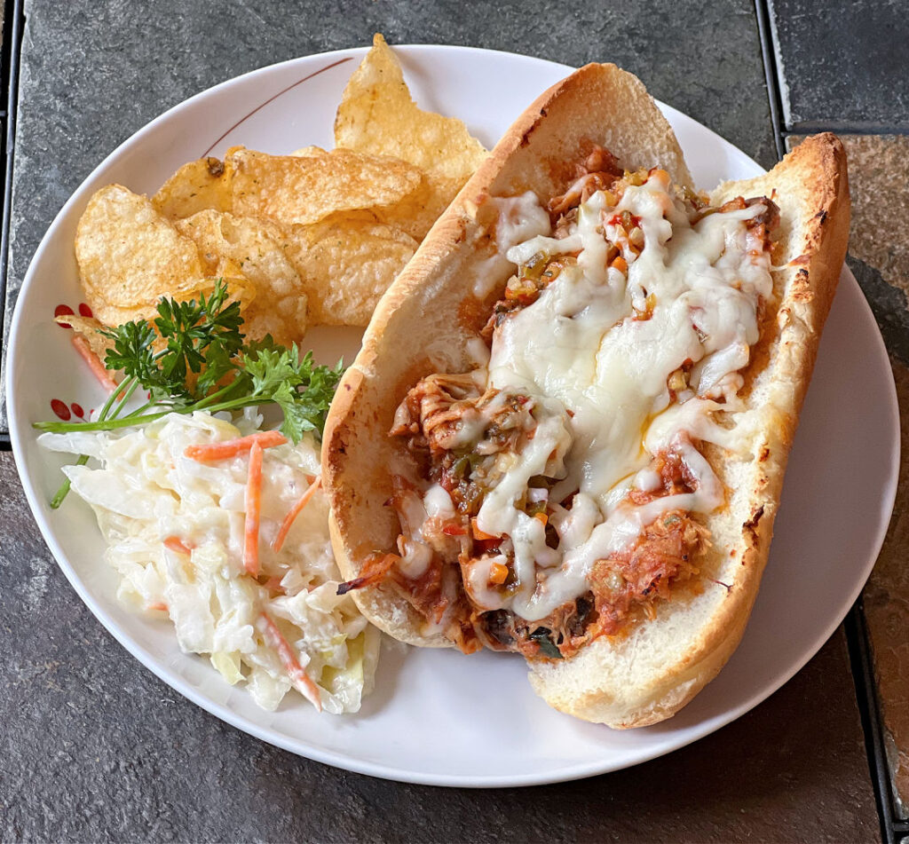 cheesy pulled italian chicken sandwich on a plate with chips and coleslaw