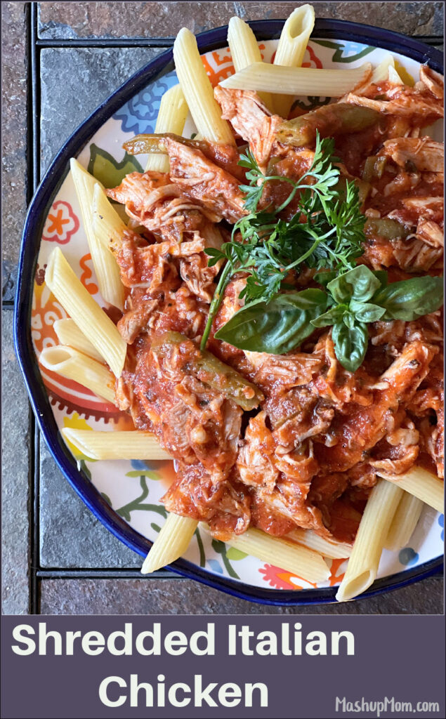 a plate of shredded Italian chicken over pasta, topped with fresh herbs
